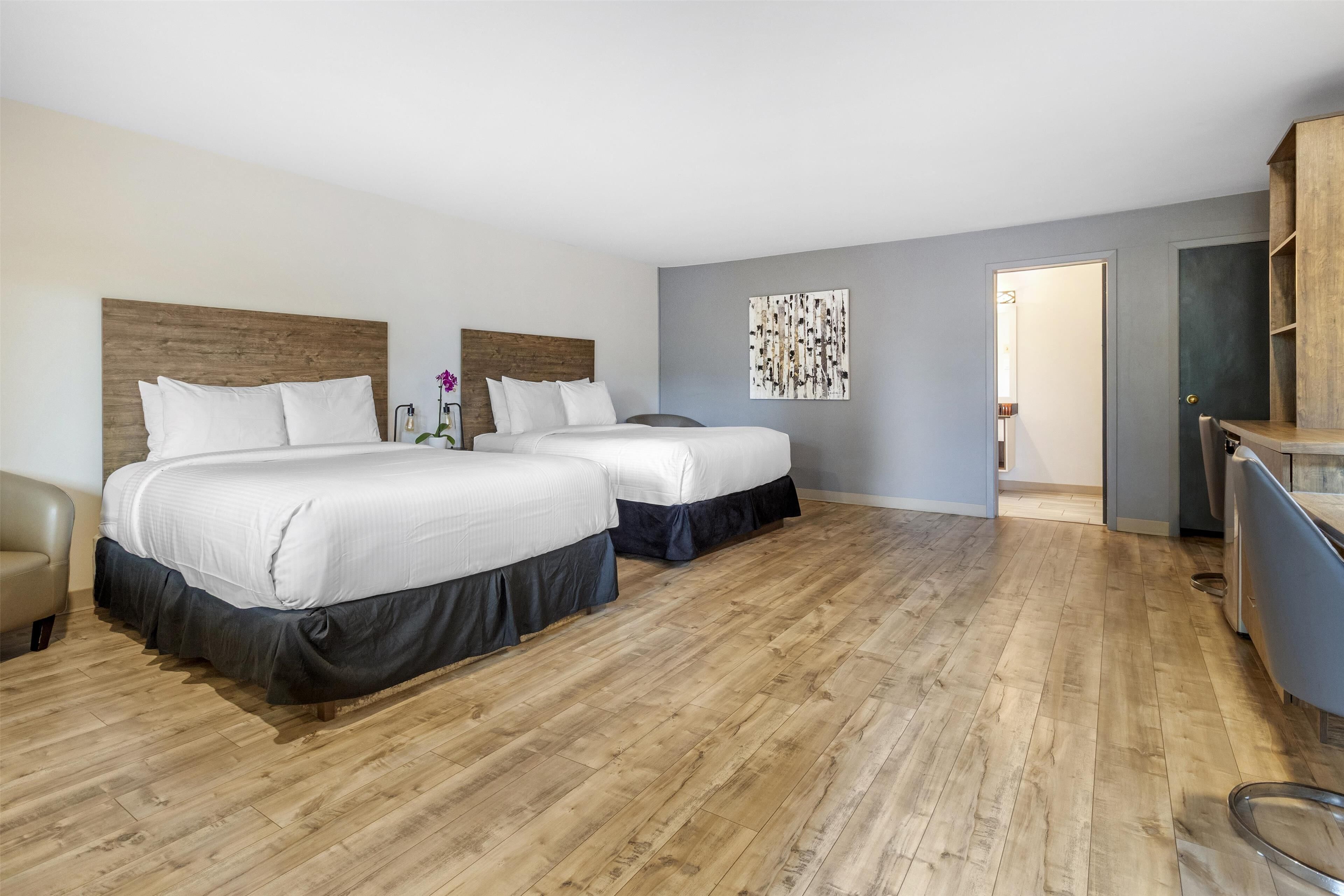 A hotel room with two beds, a wooden headboard, a grey wall with a piece of abstract art, and a wooden floor.