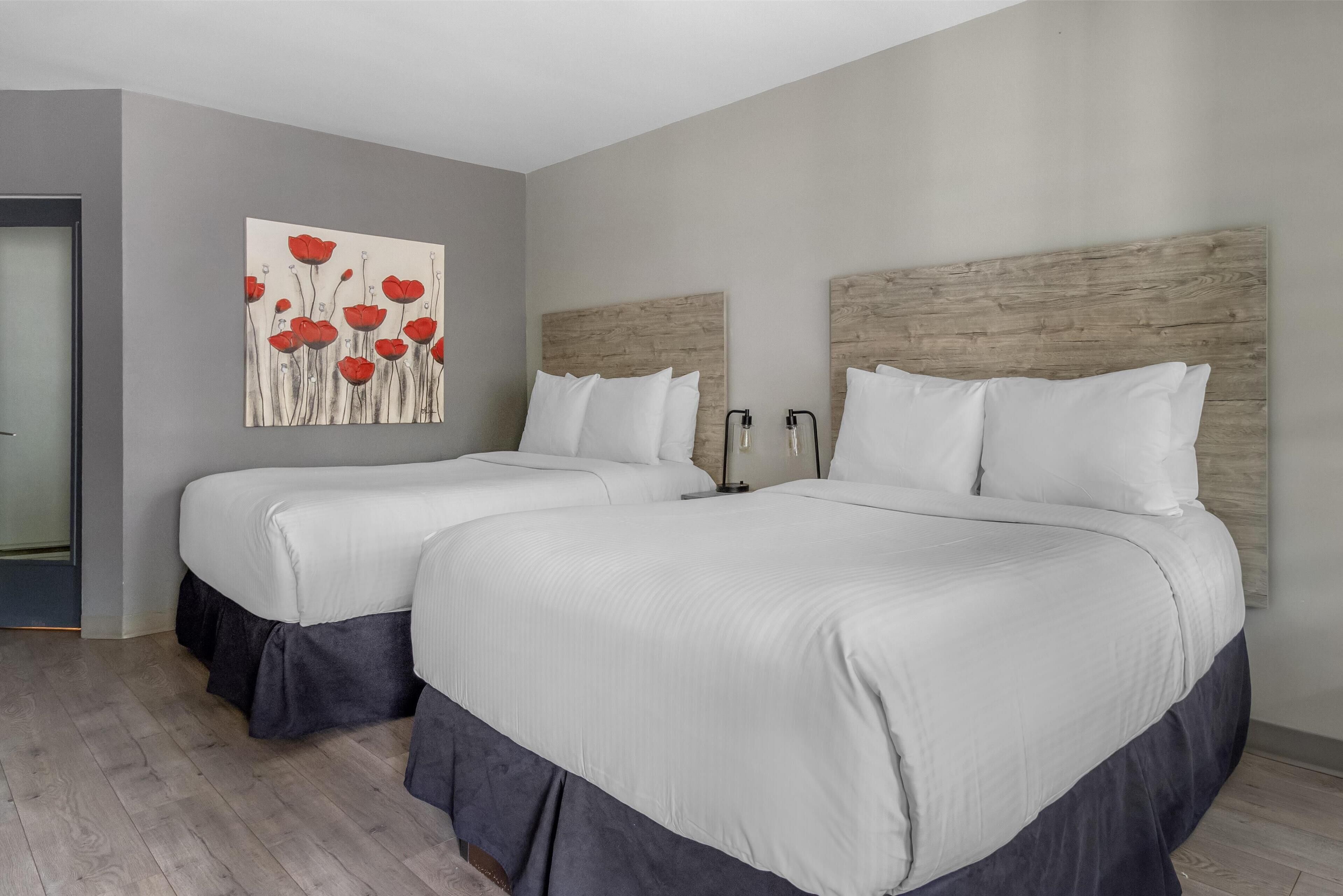 A hotel room with two beds, grey walls, a wooden headboard, and a painting of red flowers.