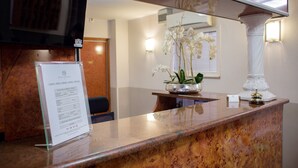 Un comptoir d’accueil avec un tableau affichant le menu, une orchidée en pot et une colonne blanche.