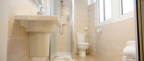 A bathroom with a shower, sink, toilet, and a window.