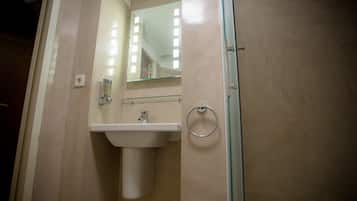 Un baño con un lavabo blanco, una cabina de ducha de vidrio y un espejo sobre el lavabo.