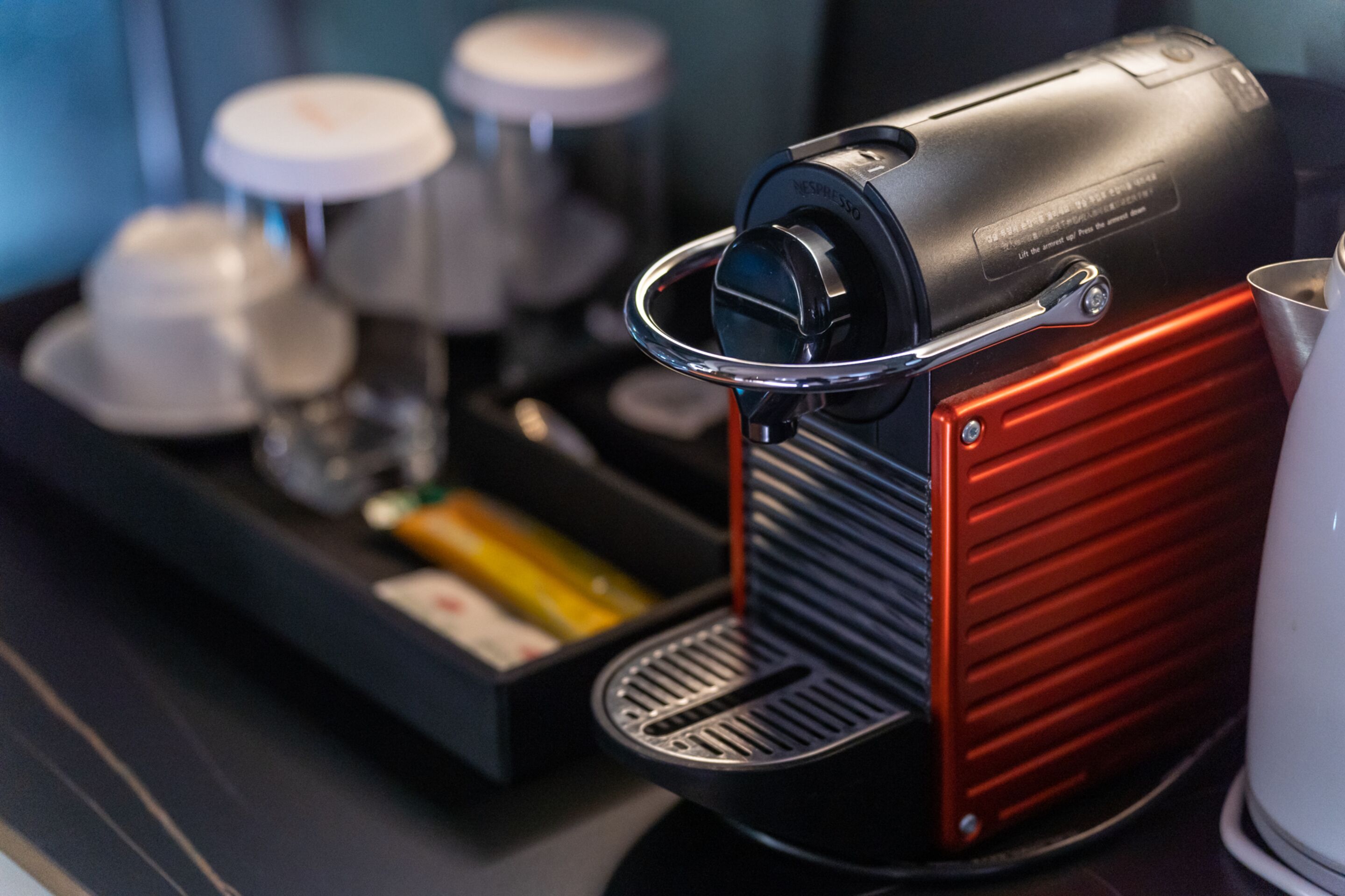 A coffee machine with a red and black design, a coffee grinder, and a tray with cups and a milk frother.