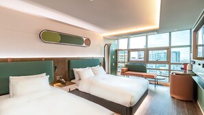 A modern hotel room with two beds, a seating area, and large windows offering a city view. - L&L Central Hotel (Jeju City)