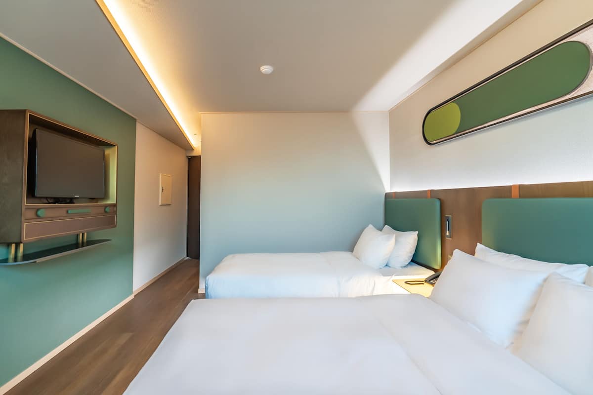 Une chambre d’hôtel avec deux lits, un téléviseur fixé au mur et un miroir au-dessus des lits.
