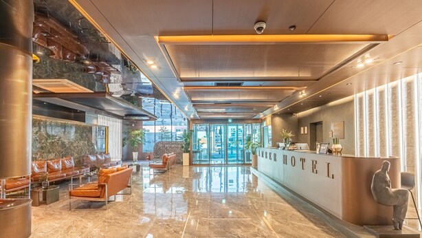 A modern hotel lobby with a reception desk, leather seating, and a view of the city. - L&L Central Hotel (Jeju City)