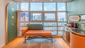 A modern room with a large window, a sofa, a small table, and a kitchenette. - L&L Central Hotel (Jeju City)