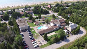 Vue aérienne d’un quartier résidentiel situé sur la côte, avec une piscine, plusieurs maisons et une plage en arrière-plan.