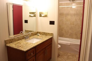 A bathroom with a granite countertop sink, wooden cabinets, a large mirror, a towel rack, and a shower area. - Sauble Beach Lodge (South Bruce Peninsula)
