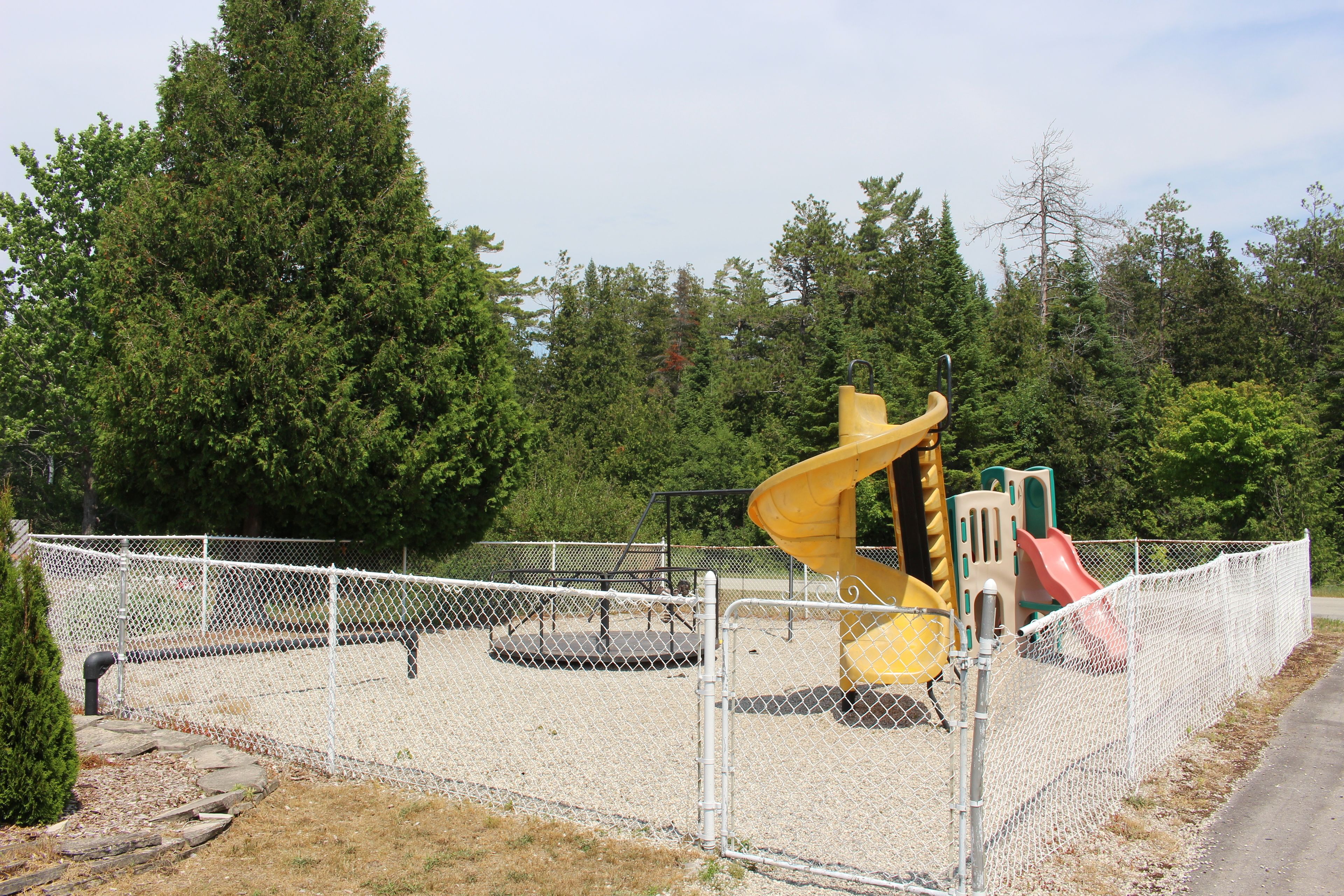A playground enclosed by a chain-link fence with a yellow spiral slide and a red slide.