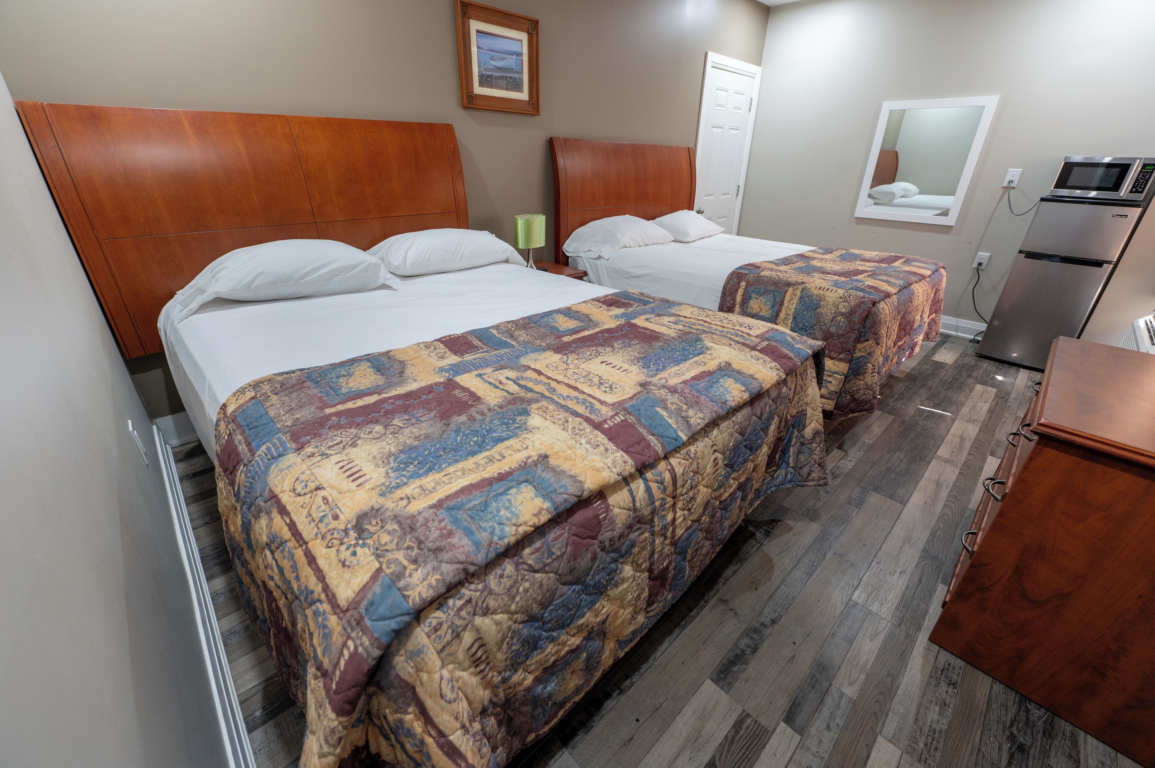 A hotel room with two beds, a wooden headboard, a microwave, and a refrigerator.