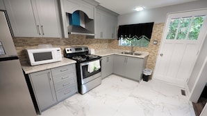 Une cuisine avec des meubles gris, un micro-ondes blanc, une cuisinière et un évier.