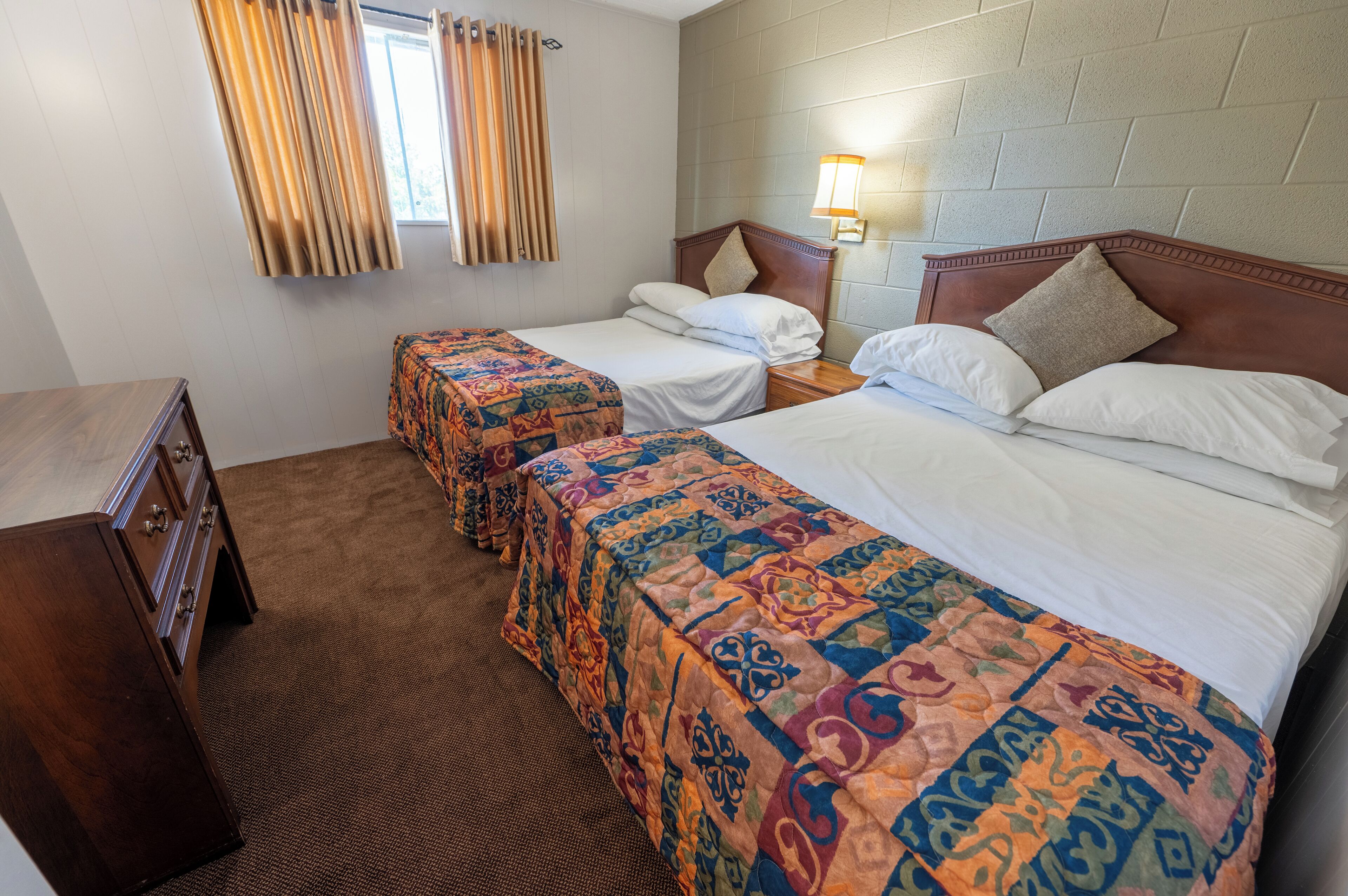 A hotel room with two beds, a dresser, a lamp, and a window with curtains.