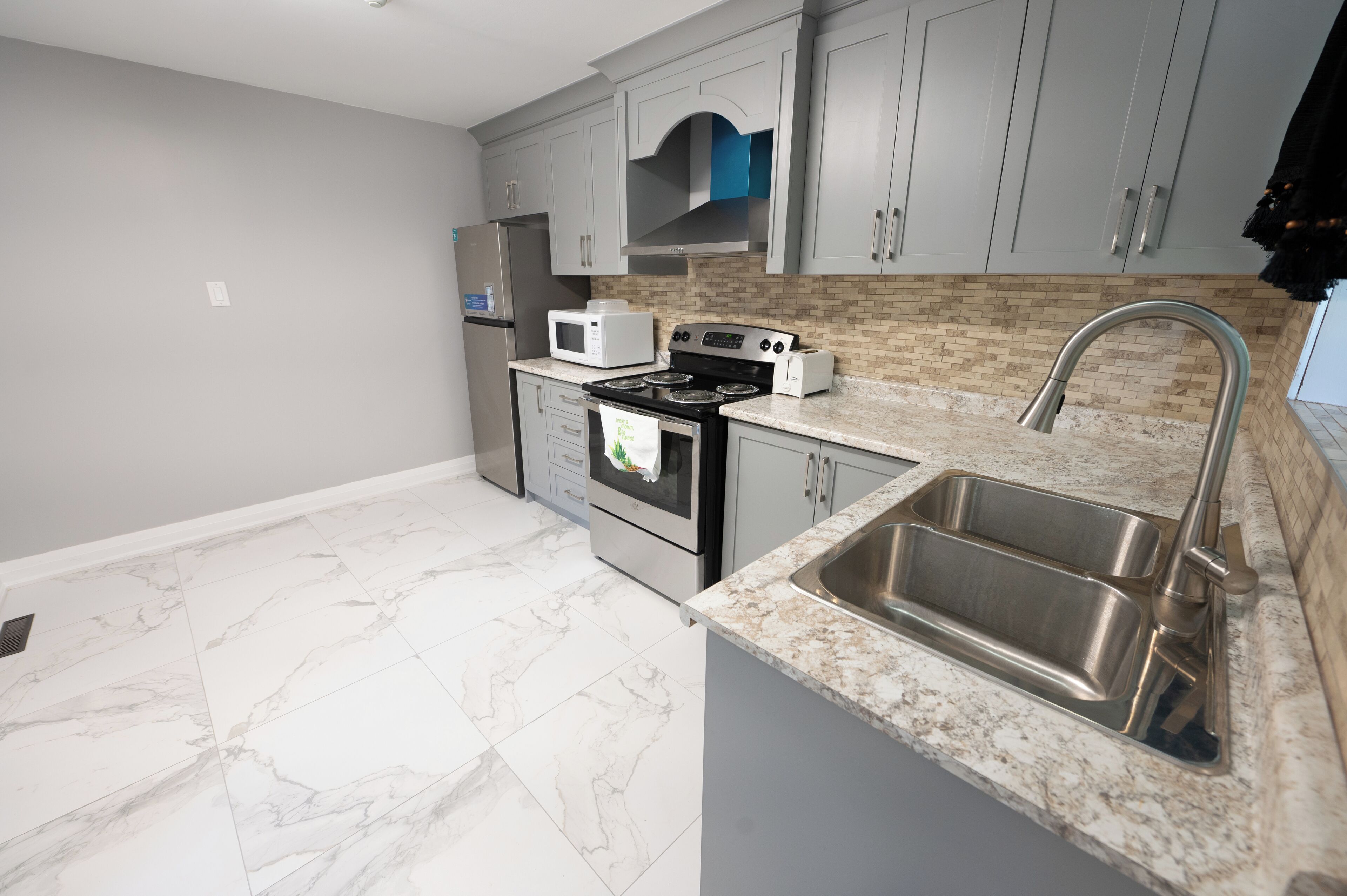 A modern kitchen with grey cabinets, a stainless steel sink, a microwave, a stove, and a toaster.