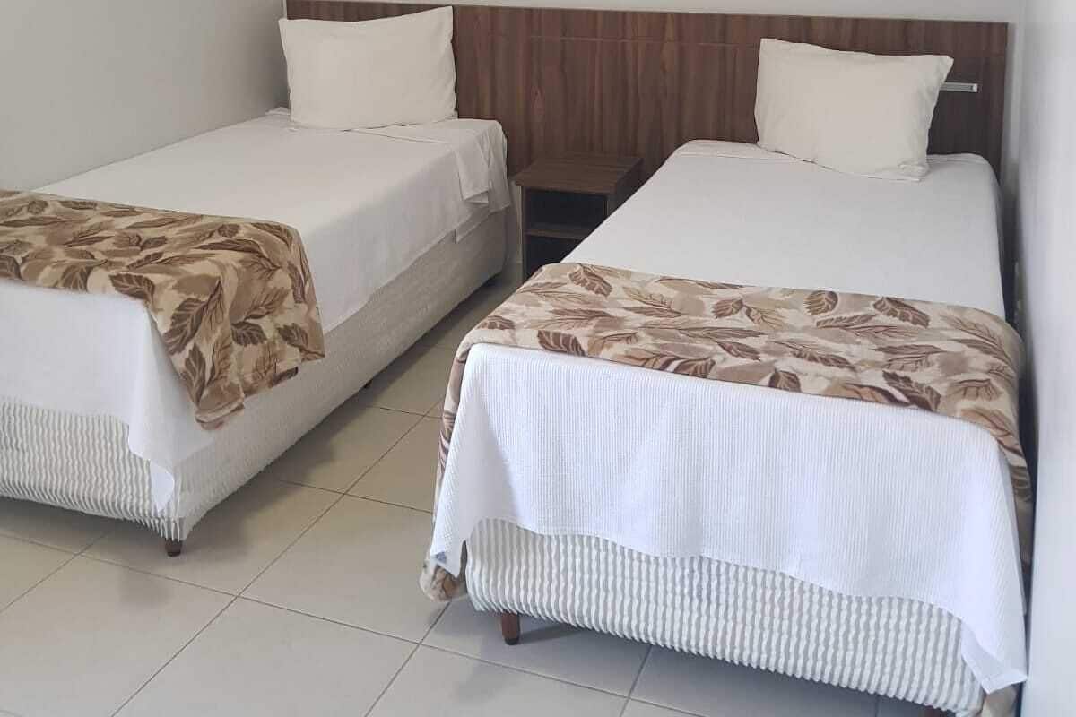 A hotel room with two single beds, a wooden headboard, a small bedside table, and a wall-mounted air conditioning unit.