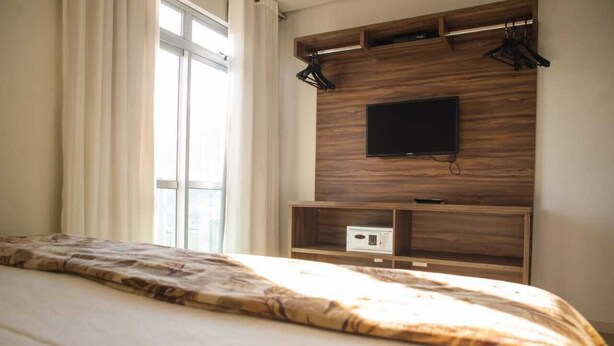 Habitación de hotel con cama, televisión montada en una pared de madera y ventana con cortinas.