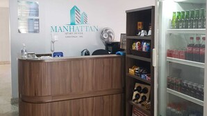 Zona de recepción de un hotel con un mostrador de madera, un cartel en la pared del Manhattan Aparthotel y un refrigerador con bebidas.