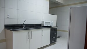 Una cocina con armarios blancos, encimera negra, microondas y refrigerador.