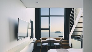 A modern hotel room with a large window, a bed, a desk with two chairs, and a TV mounted on the wall. - Poong Gyung Hotel (Seogwipo)