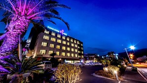 A hotel with a modern design, multiple floors, and a parking lot with several cars. - Poong Gyung Hotel (Seogwipo)