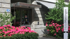 Entrada de un hotel con un letrero que dice "HotelHottingen", fachada de piedra y flores rosadas en primer plano.