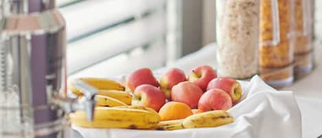 A table with a fruit bowl containing bananas and apples, a glass bottle, and jars of food.