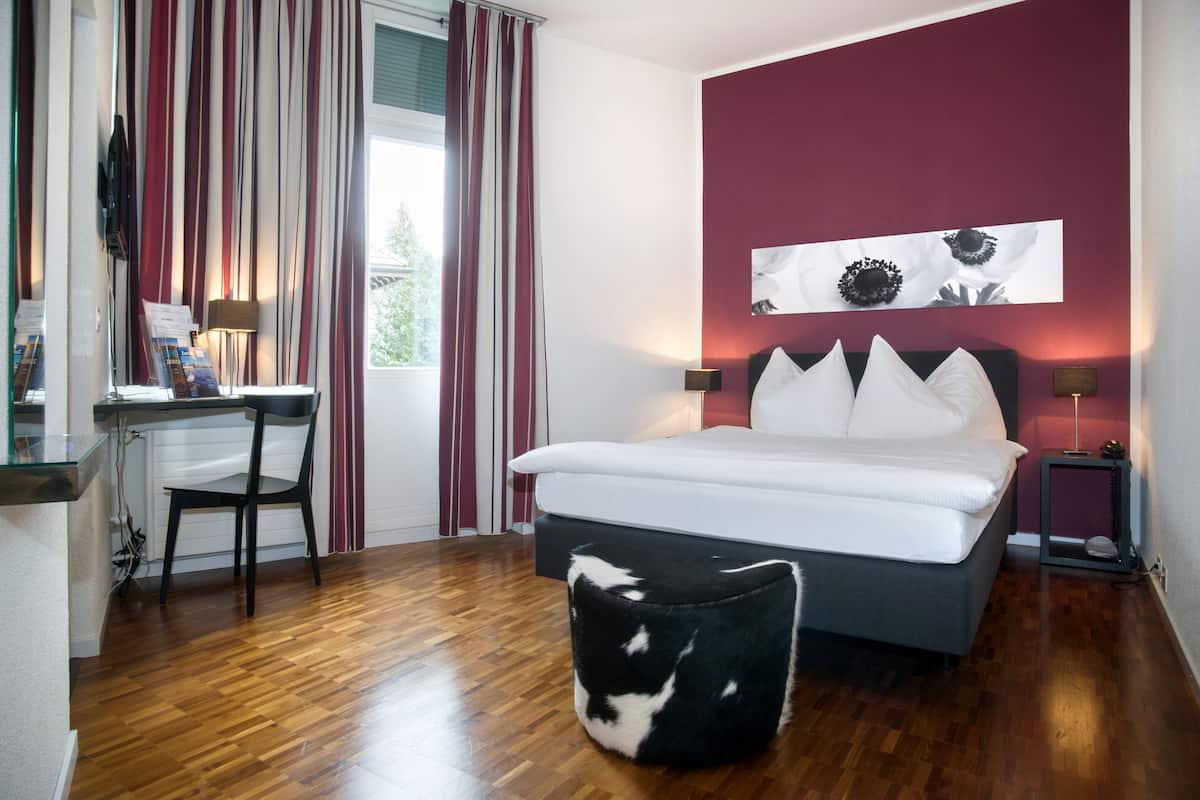 Una camera da letto con un letto, una scrivania, una sedia e un poggiapiedi.