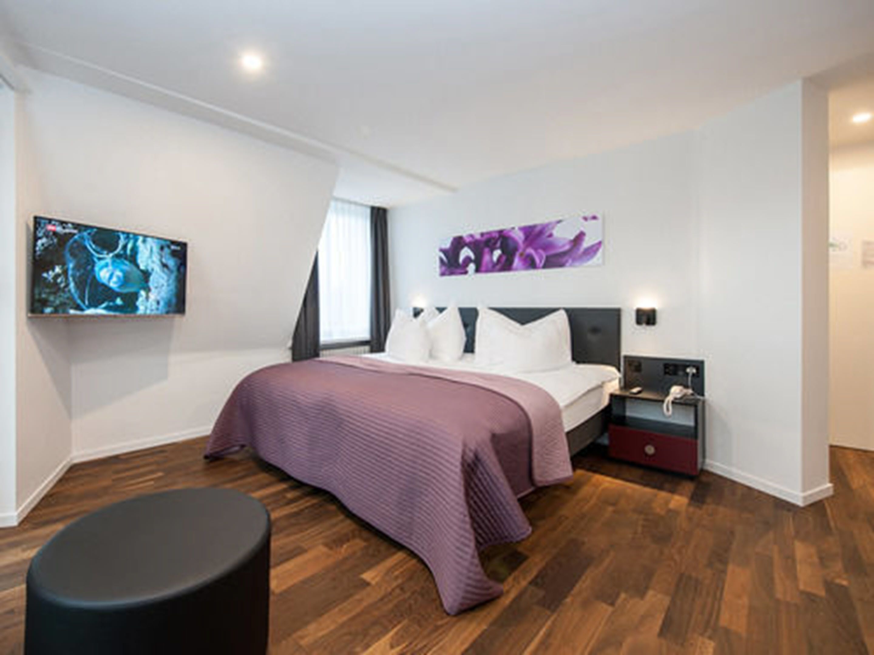 Une chambre moderne avec un grand lit, une table de chevet, un téléviseur à écran plat et une œuvre d’art accrochée au mur.