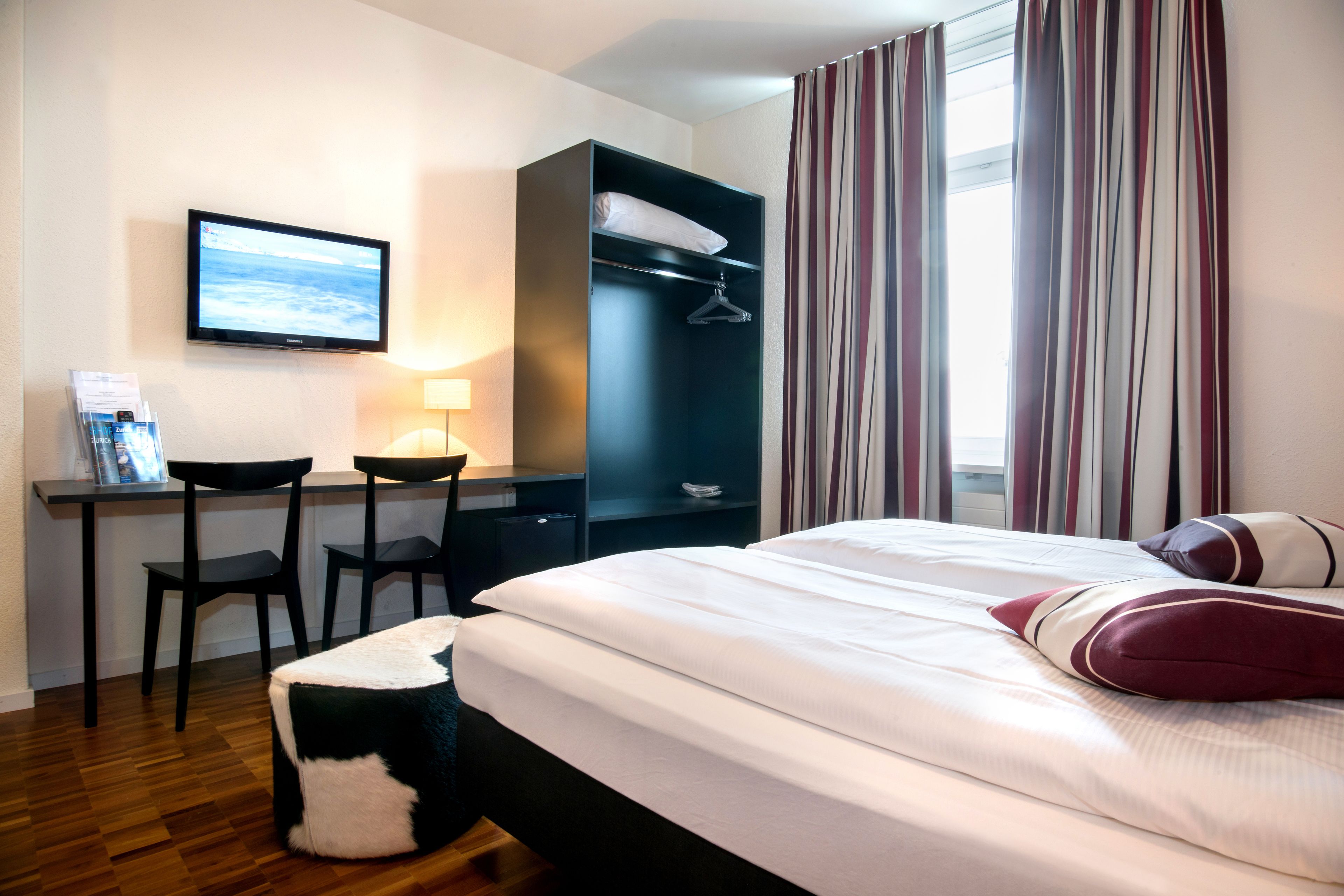 Una habitación de hotel con una cama, un escritorio con dos sillas, un televisor y un armario.