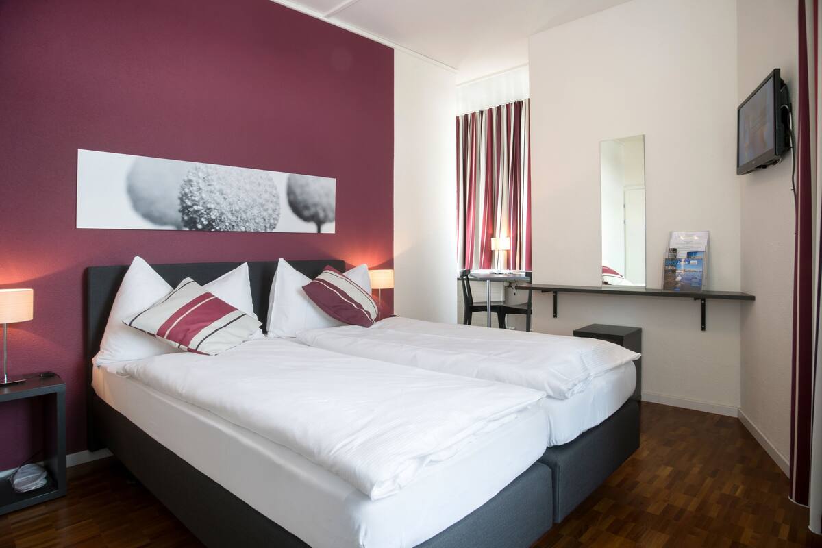 Una camera d'albergo con un letto grande, una scrivania, una sedia, uno specchio e un televisore.