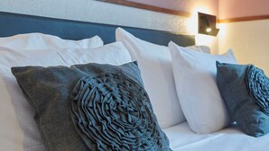 Una habitación de hotel con una cama bien hecha, ropa de cama blanca y almohadas decorativas.