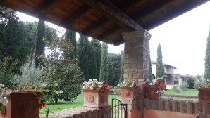 A covered patio with terracotta planters, a stone pillar, and a view of a garden with trees and a house in the background. - Residenza di Rocca Romana (Sutri)