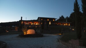 A large, multi-story building with a stone facade, multiple windows, and a well-maintained garden area with a central feature that appears to be a large, round stone structure. - Residenza di Rocca Romana (Sutri)