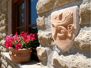 A stone wall with a coat of arms and a potted plant with pink flowers. - Residenza di Rocca Romana (Sutri)