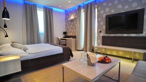 A modern hotel room with a bed, a desk, a TV, and a coffee table with fruit and glasses. - Hotel Gallus (Zagreb)