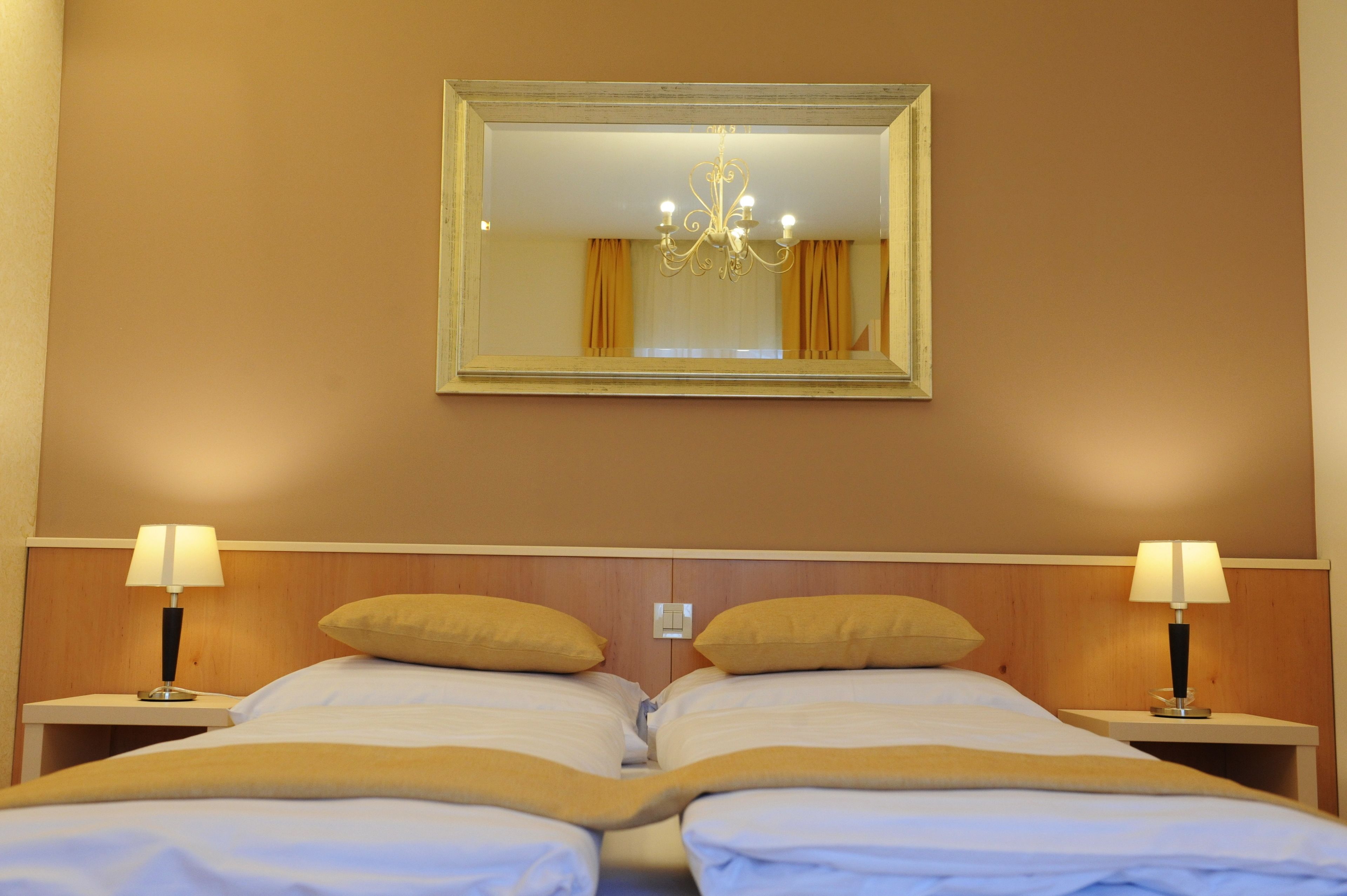 A hotel room with two beds, a chandelier, and a mirror on the wall.