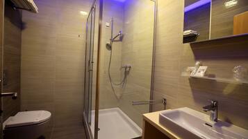 A modern bathroom with a glass-enclosed shower, a white toilet, and a sink with a mirror above it.