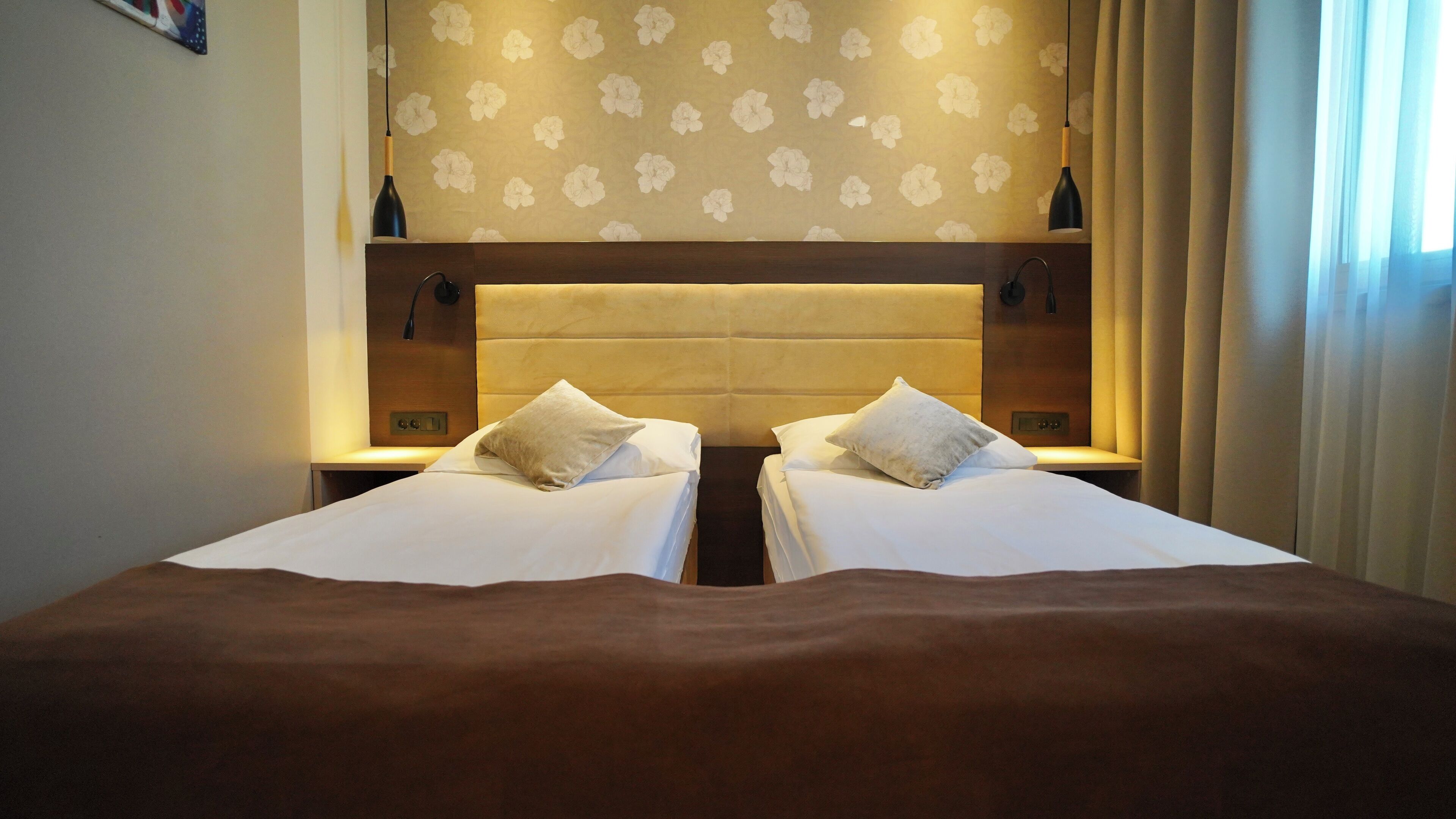 Een hotelkamer met een groot bed, twee nachtkastjes, een hoofdbord met een bloemenprint en een raam met gordijnen.