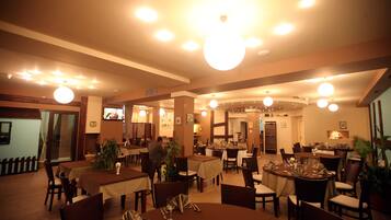 A restaurant with multiple tables and chairs, a wooden floor, and ceiling lights.