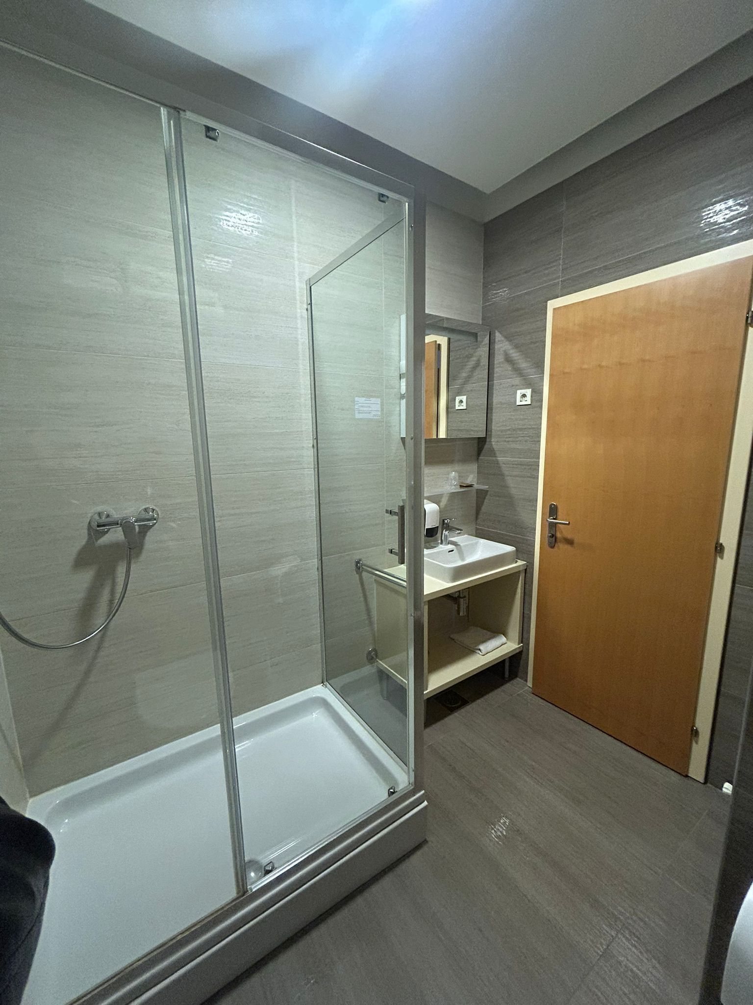 Un baño moderno con cabina de ducha de vidrio, un lavamanos y una puerta de madera.