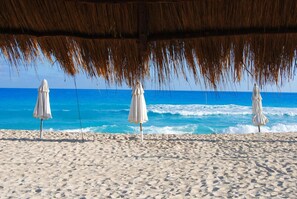 Une plage avec trois parasols blancs placés sous un toit de chaume, donnant sur l’océan.