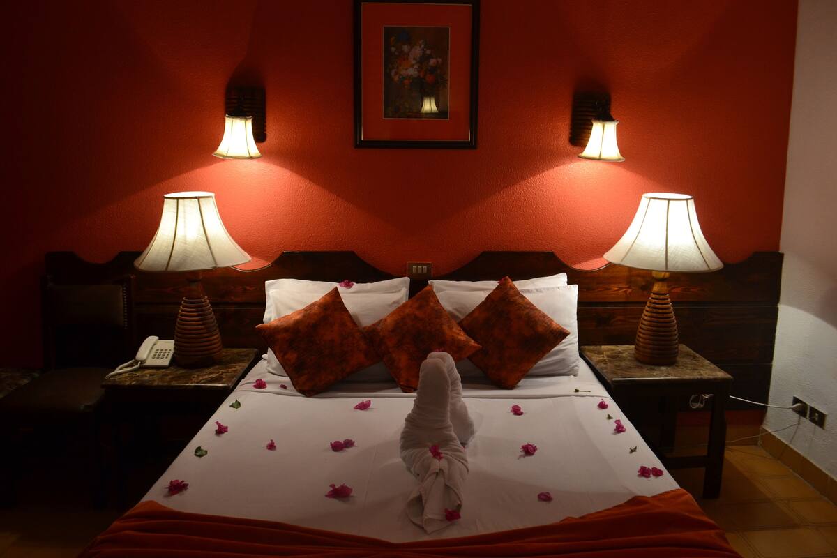 A hotel room with a bed, two bedside lamps, a telephone, and a painting on the wall.