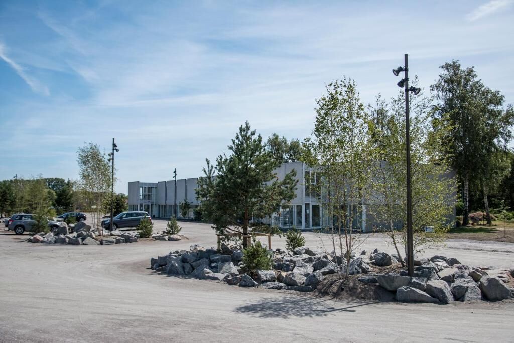 A parking lot with modern buildings, a few trees, and a clear sky.