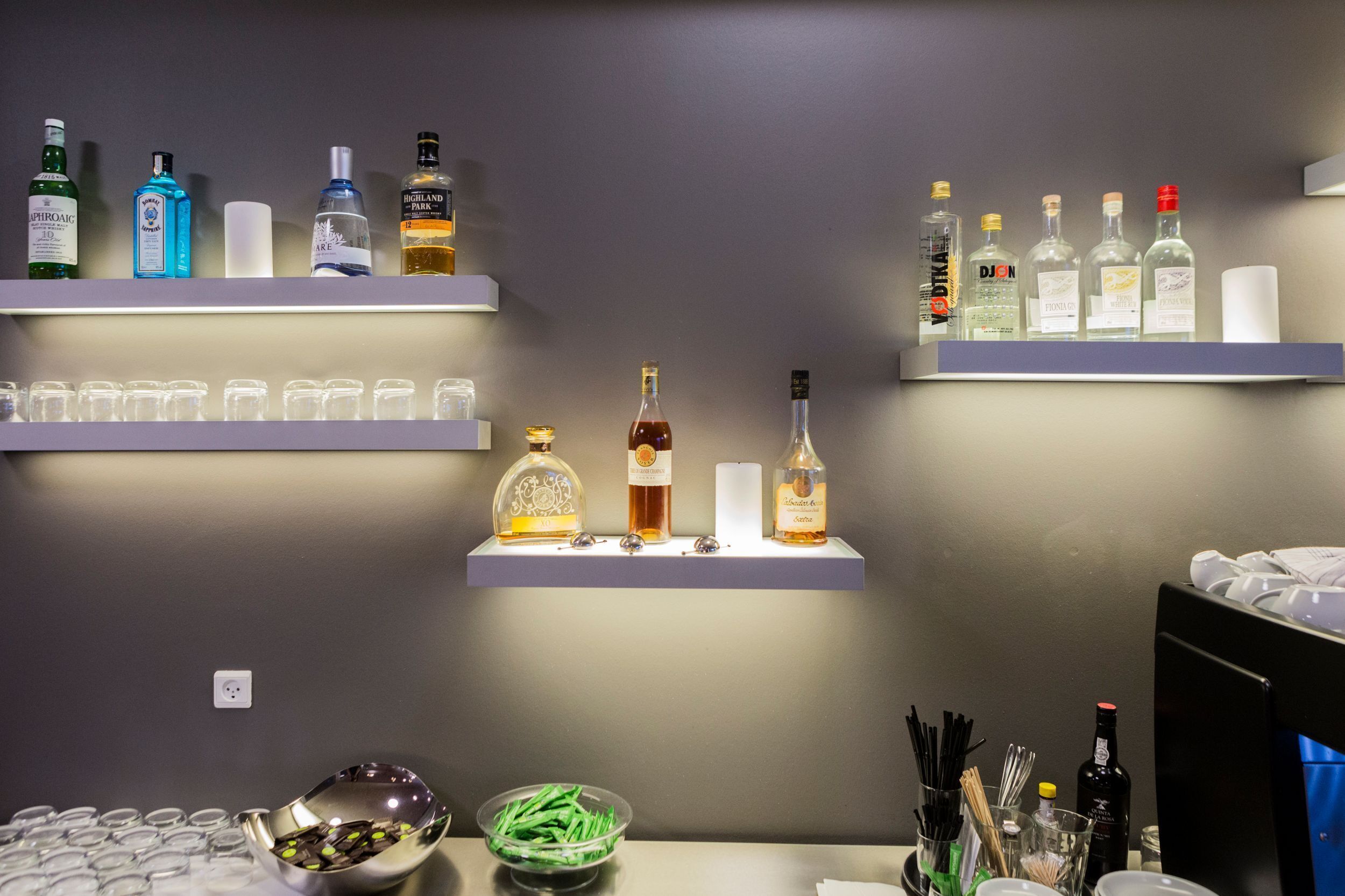 A bar area with shelves of liquor bottles, a bowl of snacks, and a glassware set.
