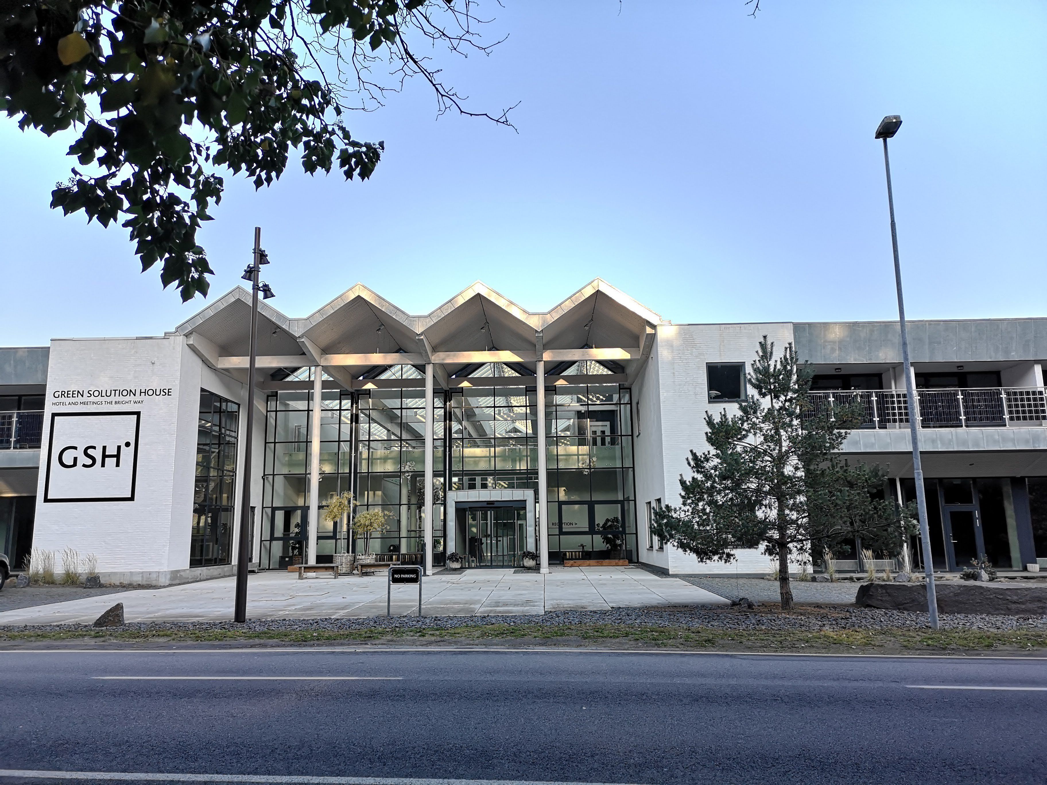 A modern building with a glass facade and a sign reading "GREEN SOLUTION HOUSE HOTEL AND MEETINGS THE BRIGHT WAY".