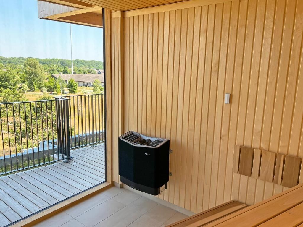 Een balkon met een houten vloer, een zwarte airconditioning en uitzicht op een woonwijk.