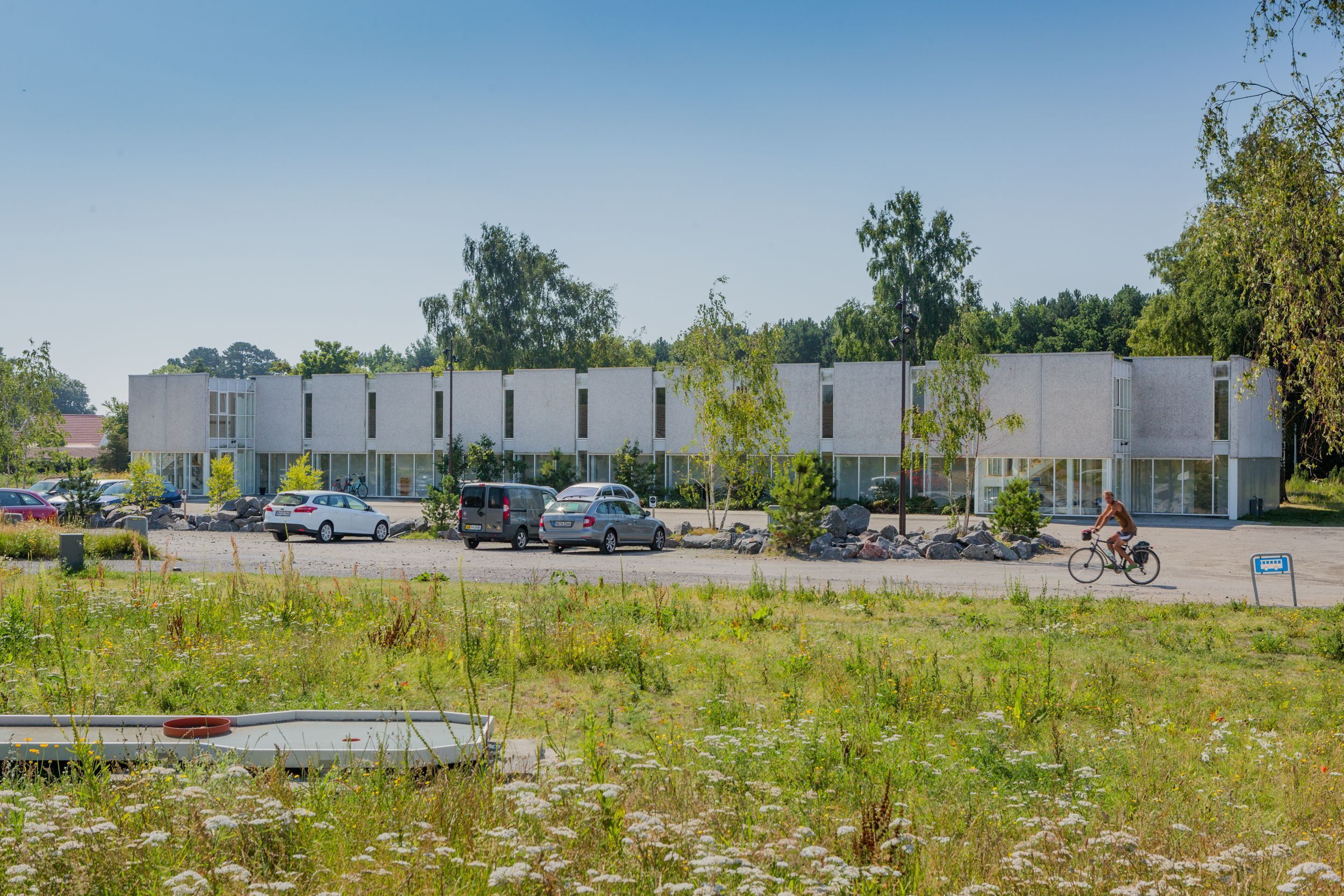 Een modern gebouw met een parkeerplaats en een fietser.