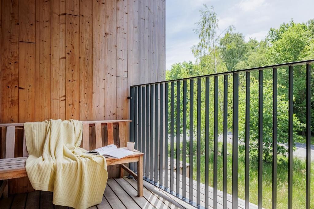 Une terrasse en bois avec un banc et une table, donnant sur une route et sur un espace verdoyant.