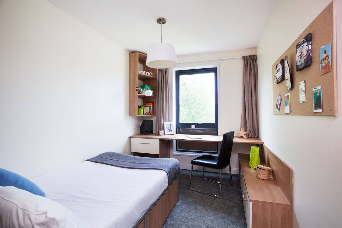 A hotel room with a bed, desk, chair, and a window with curtains.