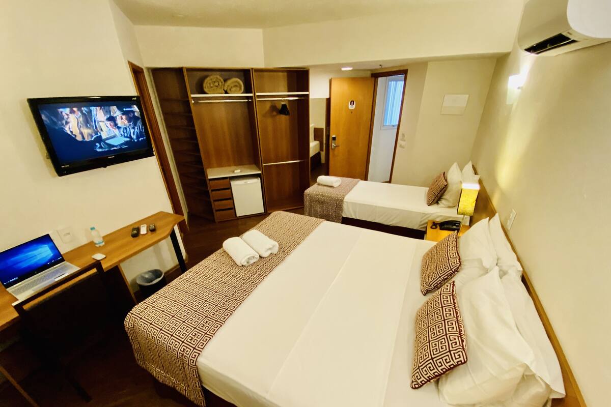 A hotel room with two beds, a desk with a laptop, a television, and a wardrobe.