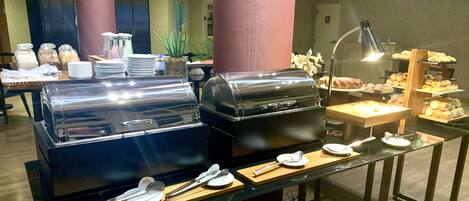 A buffet setup with two large food warmers, serving utensils, and a variety of food items on display.